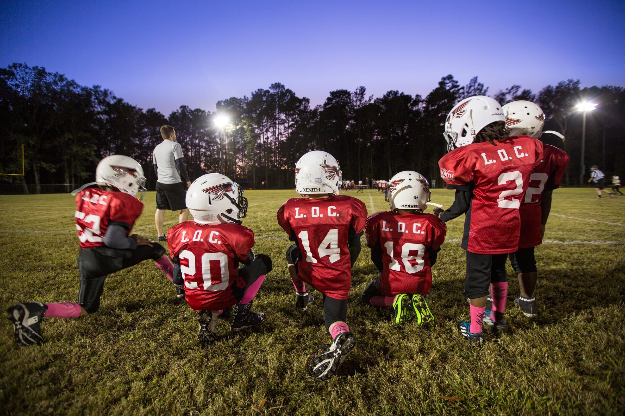 North Charleston youth football players kneeling on the field under the lights at dusk